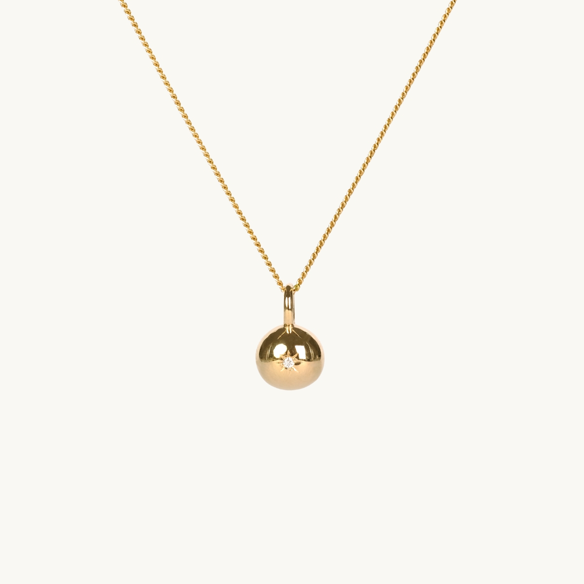 A round pendant in gold with a white diamond on a gold chain