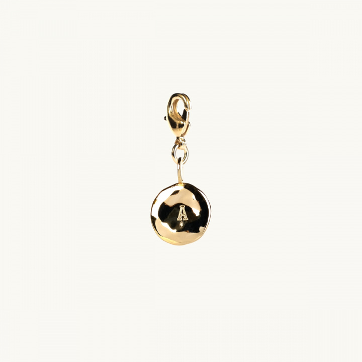 A letter coin in gold with an organic shape. 