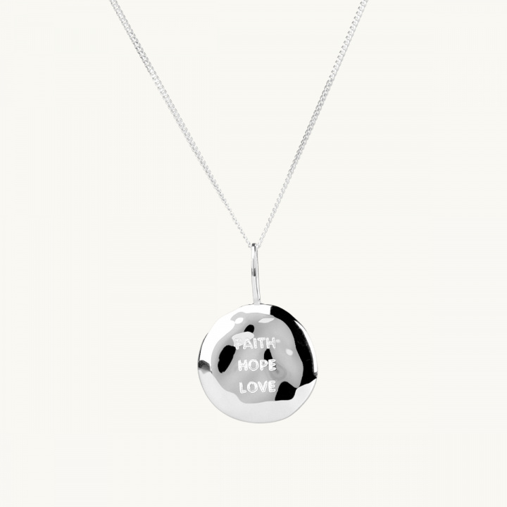 A coin in silver with an organic shape and the engrave faith, true, love