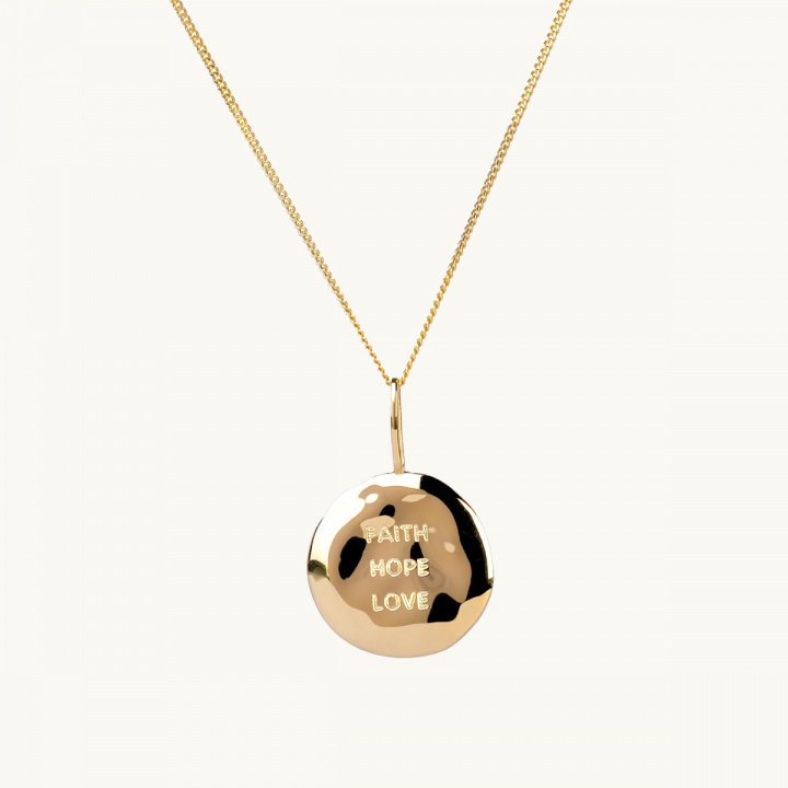 A coin in gold with an organic shape and the engrave faith, true, love